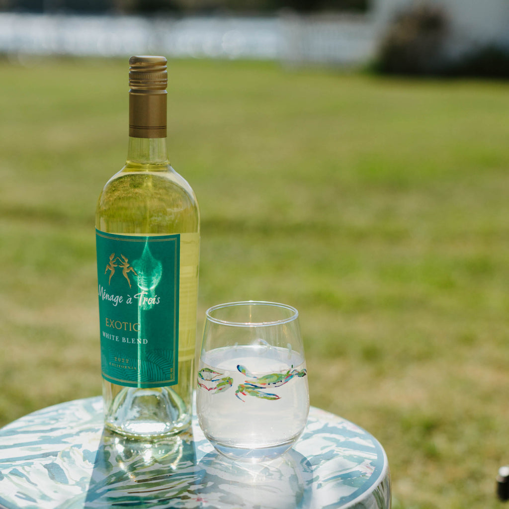 Bottle of white wine and a glass on a floral-patterned table outdoors.