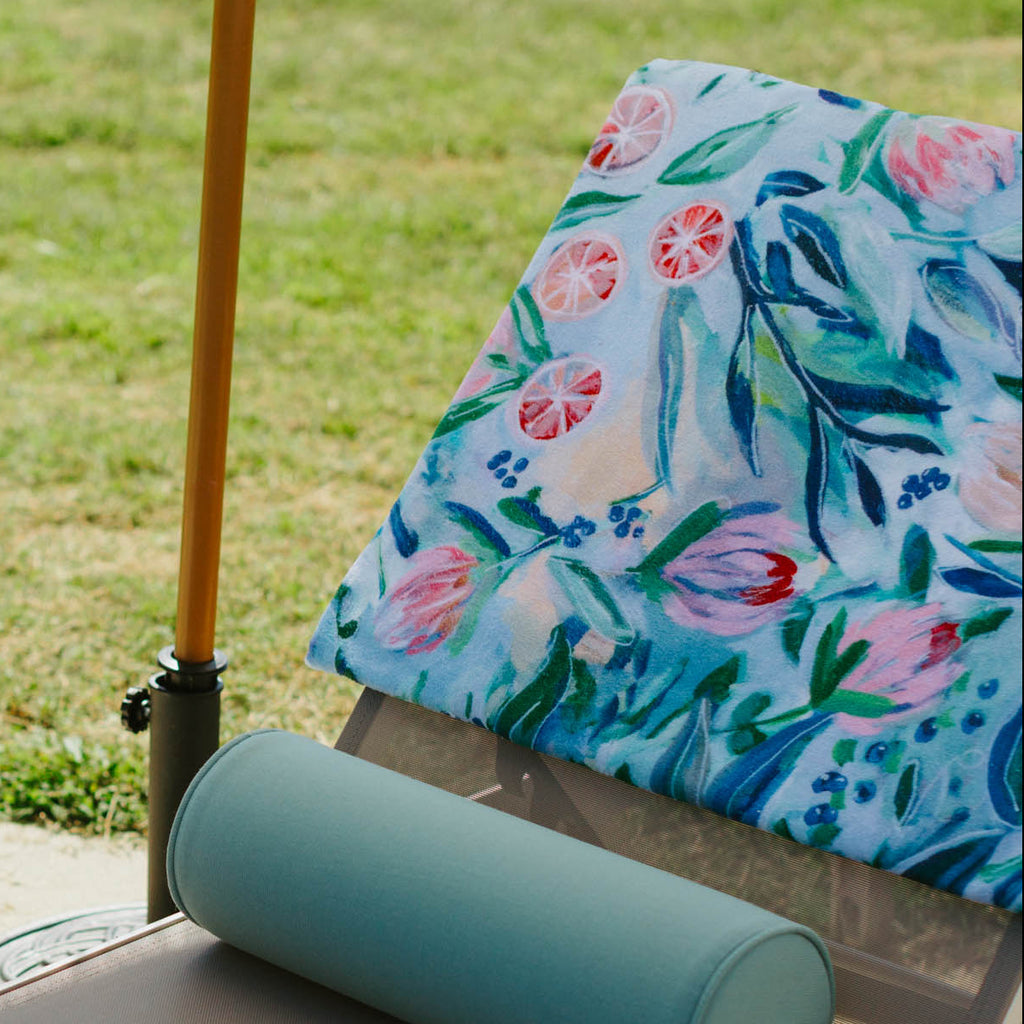 Chaise lounge with a bottle, glasses, and books on a grassy outdoor setting