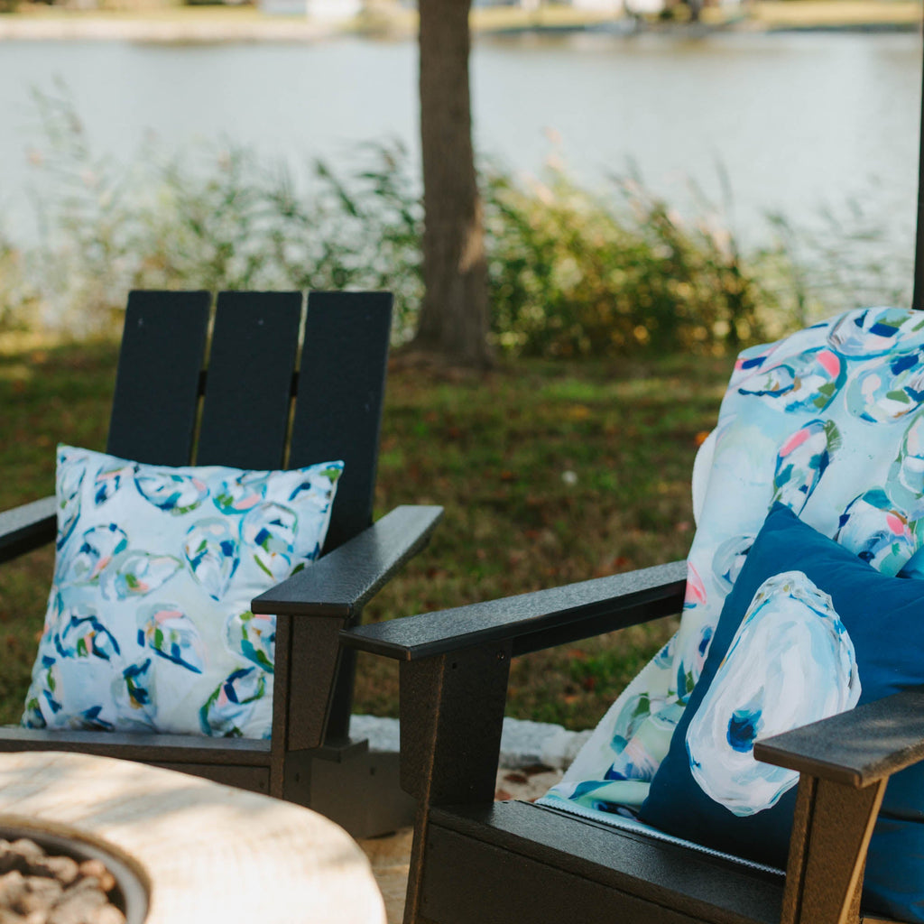 Two Adirondack chairs with decorative pillows by a lake.