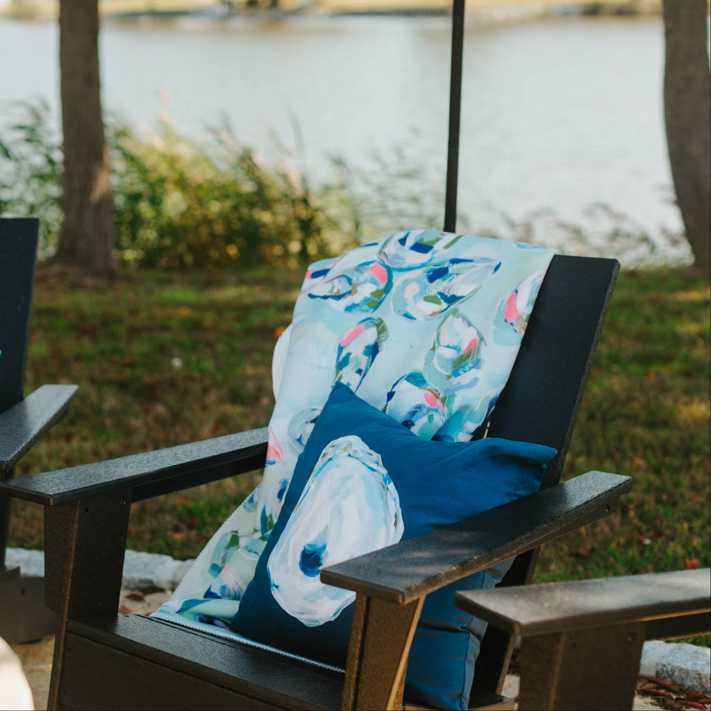 Two Adirondack chairs with decorative pillows by a lake.