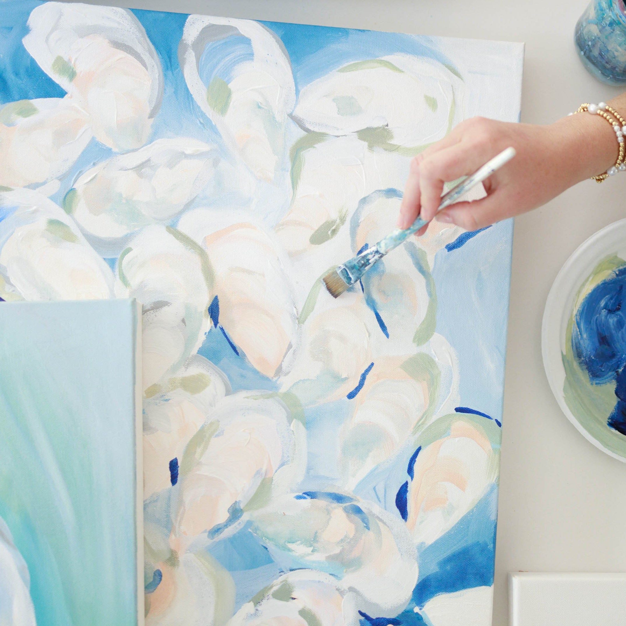 Person painting abstract art on a canvas with blue and white colors.
