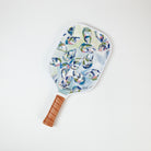 A pickleball paddle with a multicolored artistic oyster design on the surface and a brown grip handle.