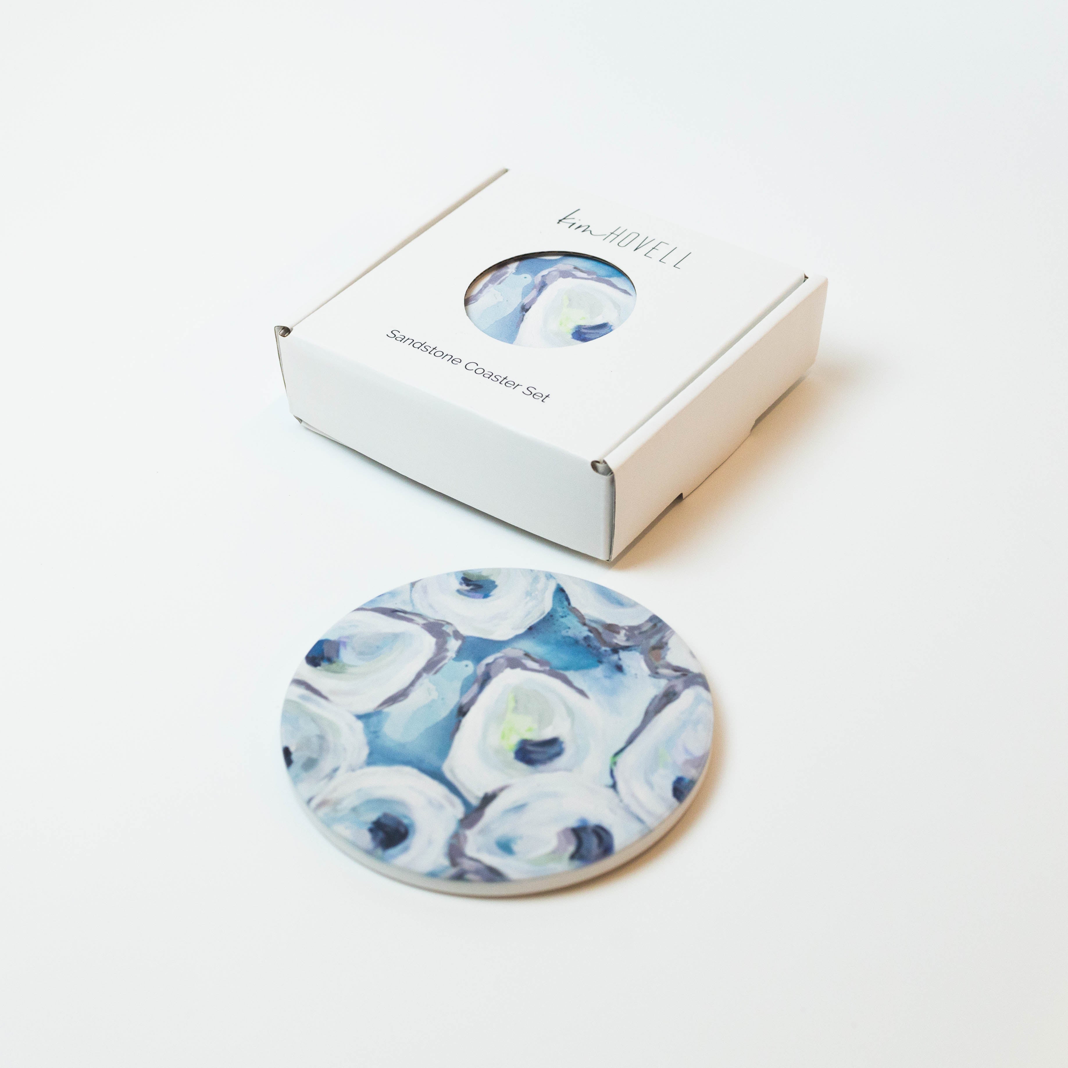 Kim Hovell Ebb and Flow blue and white oyster pattern design on a sandstone coaster next to box packaging 