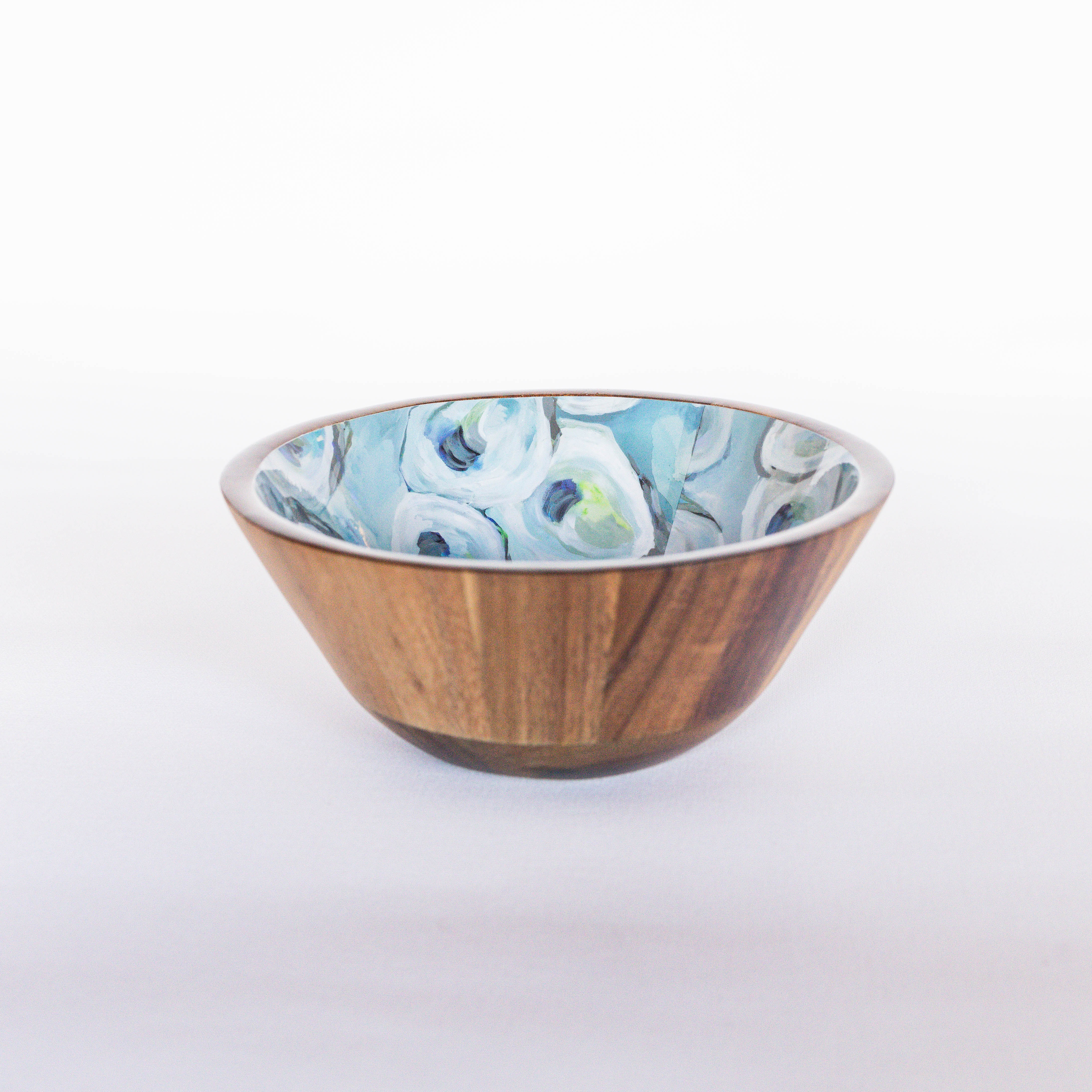 A medium-sized wooden bowl with blue and white oyster patterned interior designed by Kim Hovell, placed against a white background.