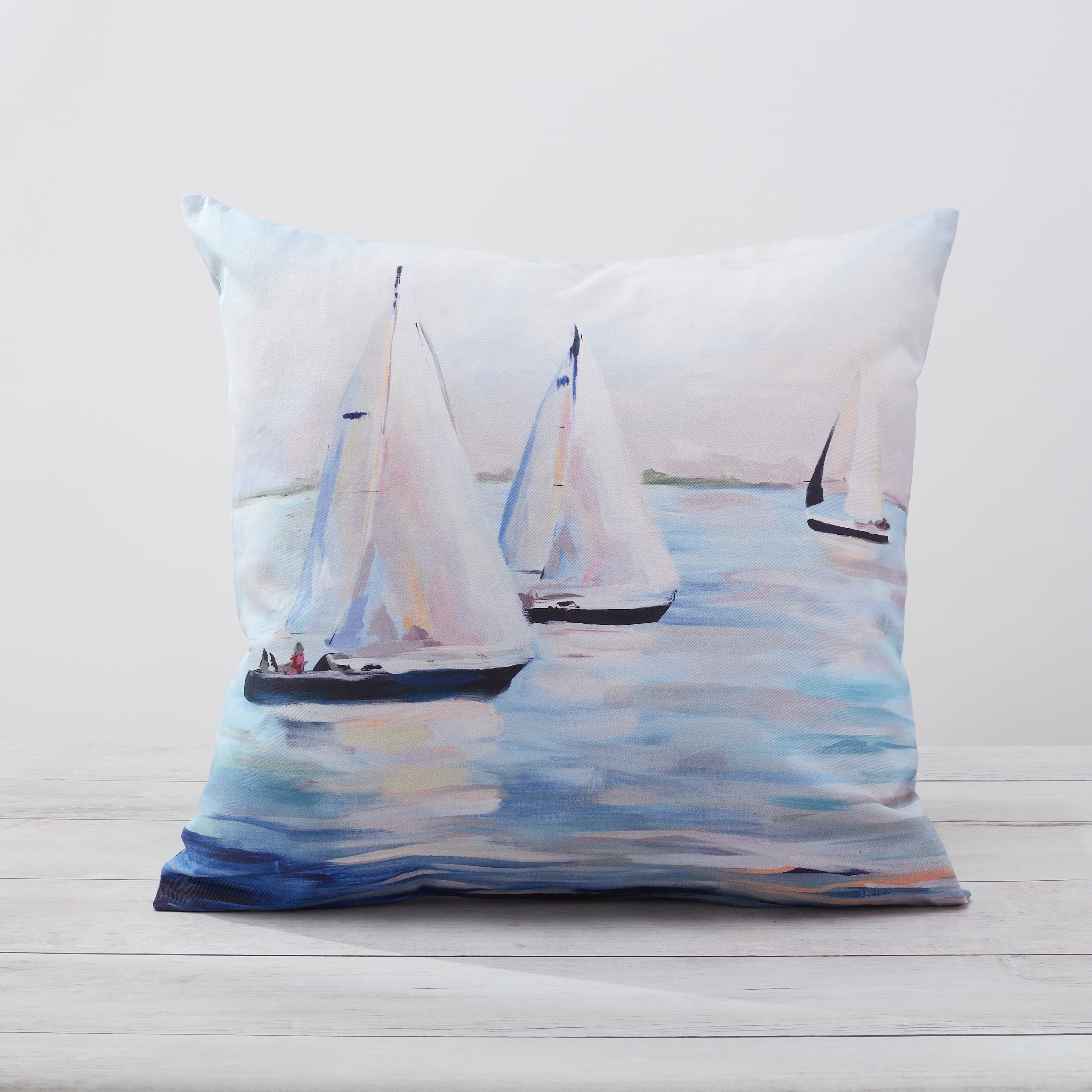 A square-shaped pillow cover with a printed sailboat design on a calm water background, laid flat on a wooden surface.