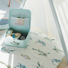 Small turquoise suitcase on a Kim Hovell cream baby blanket with colorful crab patterns