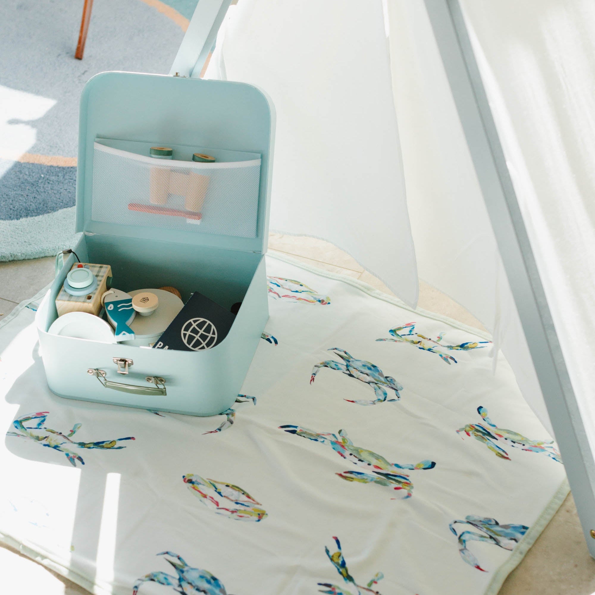 Small turquoise suitcase on a Kim Hovell cream baby blanket with colorful crab patterns