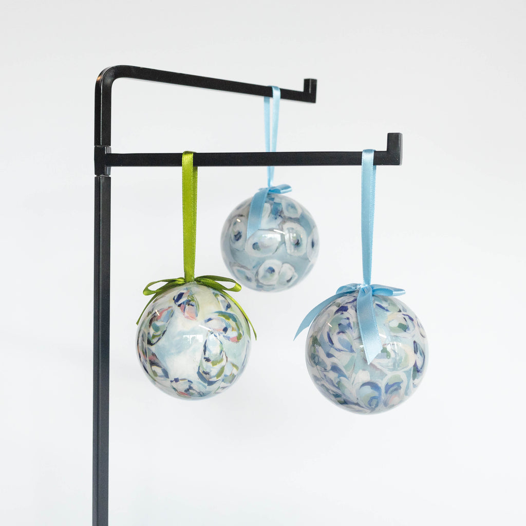 A set of three Kim Hovell round ornaments with a shell pattern in blue white, and green, hanging from ribbons.