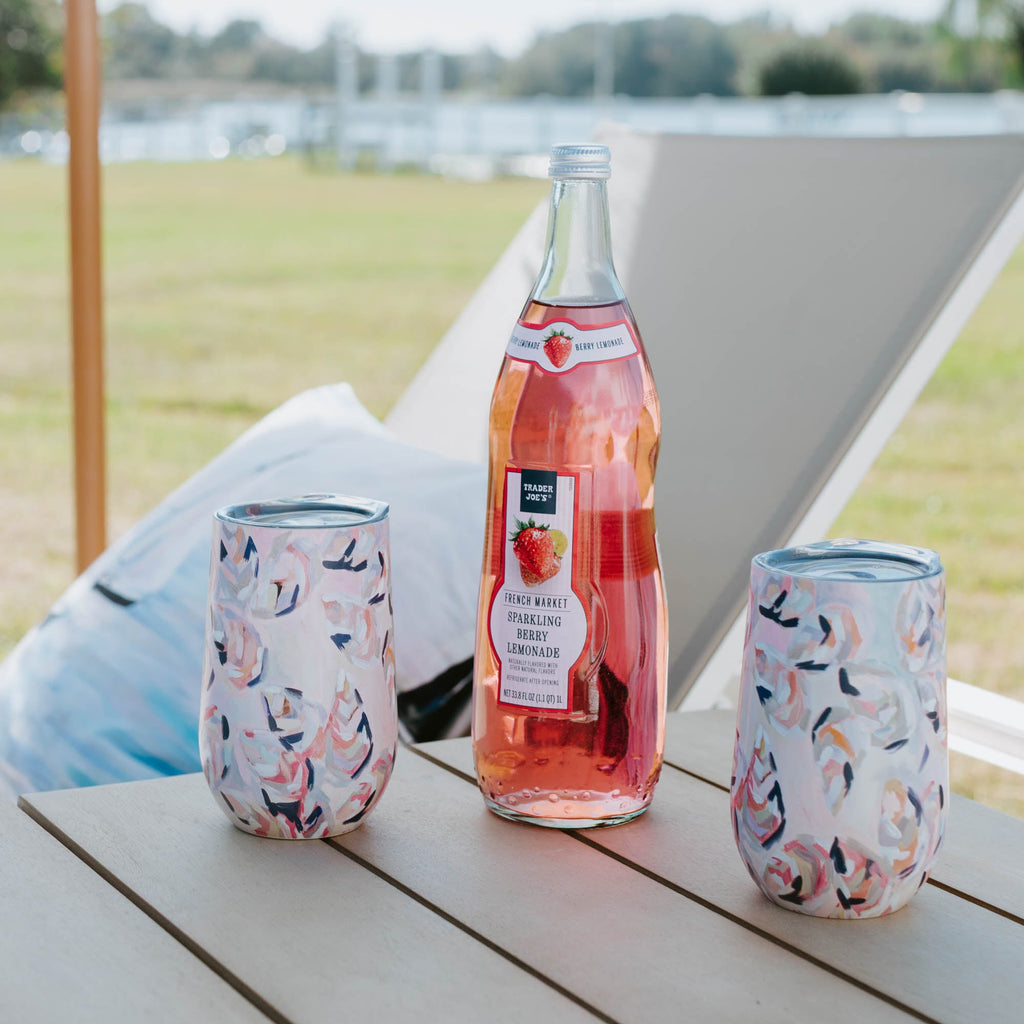 Two Kim Hovell peach gems shell-patterned wine tumblers with a bottle of strawberry lemonade on an outdoor wooden table 